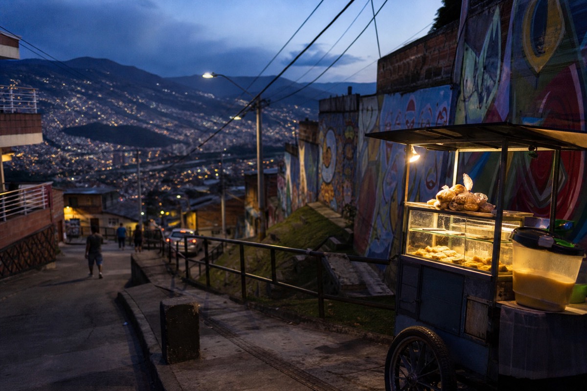 Street food stall with empanadas and mango ice cream beside a mural-covered wall in Comuna 13