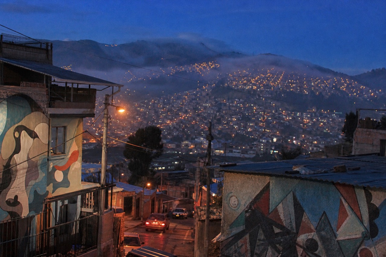 A hillside neighbourhood at dusk seen from a terrace, thousands of small window lights stacked up the slope, deep blue sky above the valley
