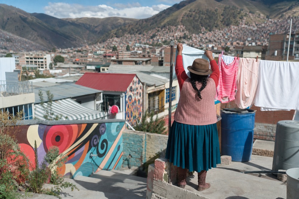 Woman seen from behind hanging laundry on a rooftop terrace above painted houses, washing lines and water tanks around her