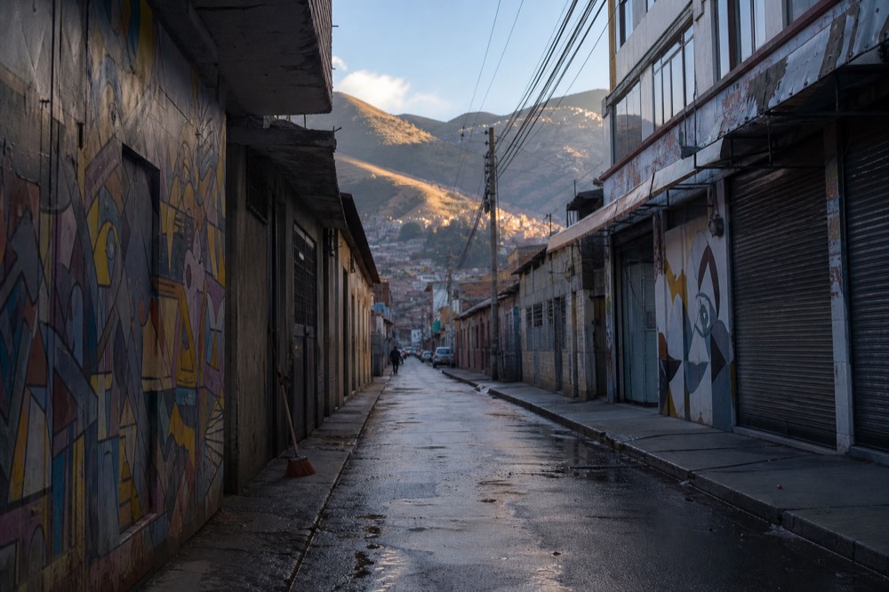 Quiet early morning alley with closed metal shutters, wet pavement and abstract murals catching the first low sunlight