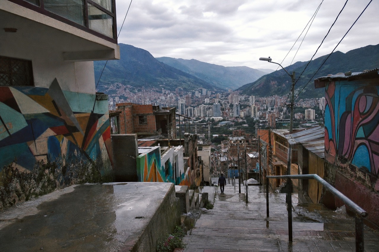 Wide daytime view over a valley city with high-rise towers on the flat floor and steep green mountains rising on both sides