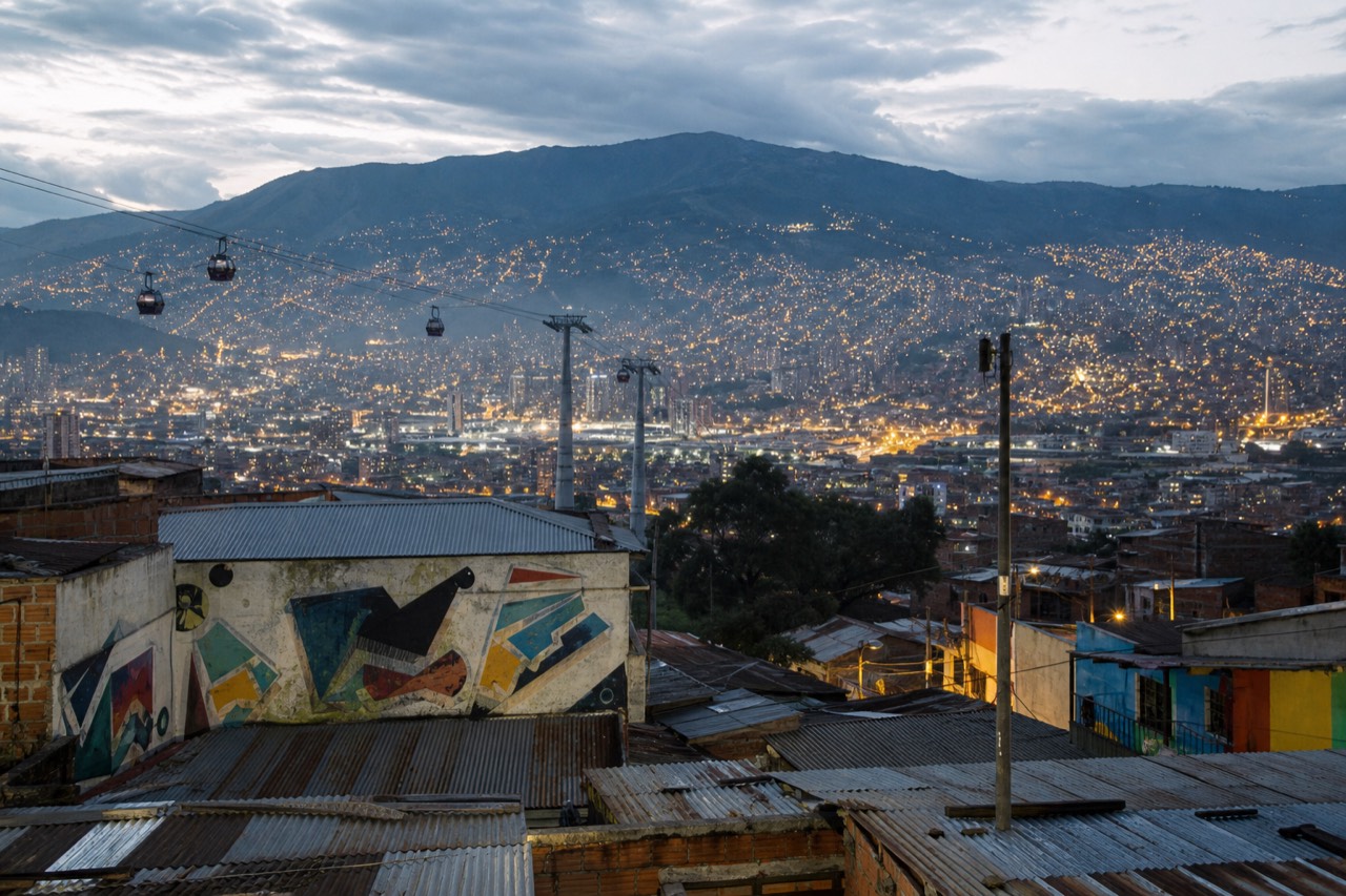 Wide view of Medellin filling its valley at dusk with cable car lines crossing the hillside and lights spreading up the slopes
