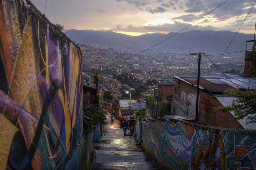 Wide valley panorama at dusk showing Medellin spread between mountain ridges, dense hillside neighbourhoods glowing on the western slope