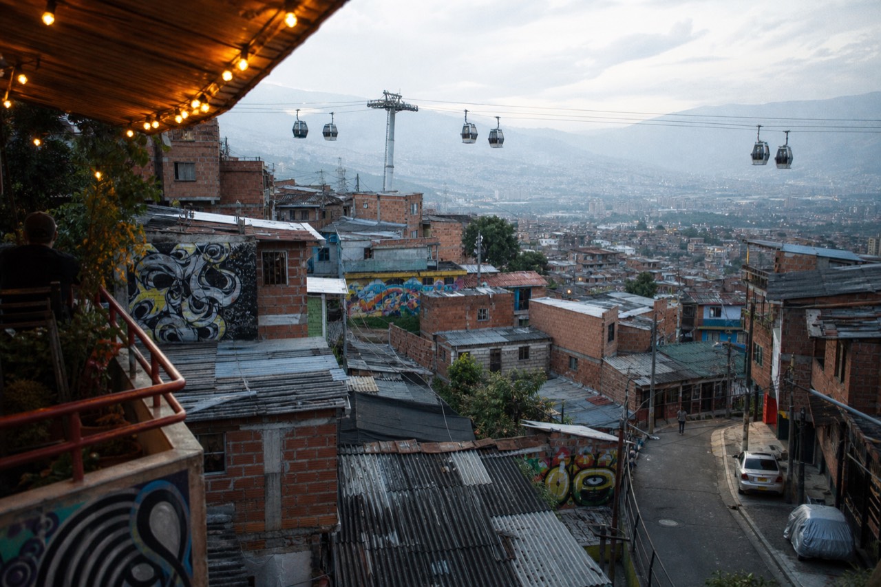 Aerial view over a steep western hillside of tightly packed brick houses in Medellin with a cable car line crossing above them in clear afternoon light