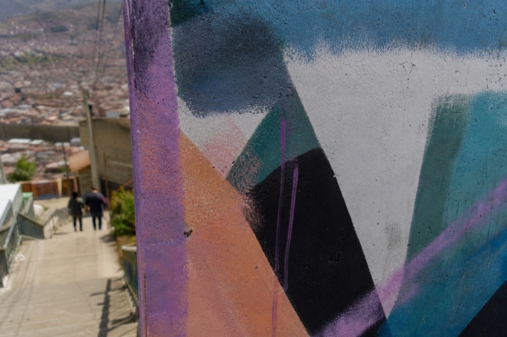 Close-up of a spray-painted concrete surface showing layered colours, drips and roller marks with fresh overspray along one edge