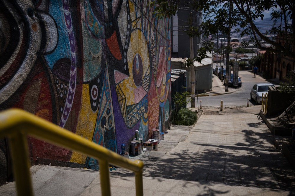 Wall of layered abstract spray-paint murals with a few used paint cans resting on the ground below, midday shade