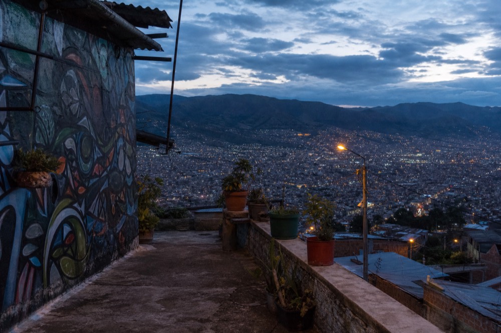 Hillside terrace viewpoint with a low wall, potted plants and a wide view over a valley city under scattered afternoon cloud